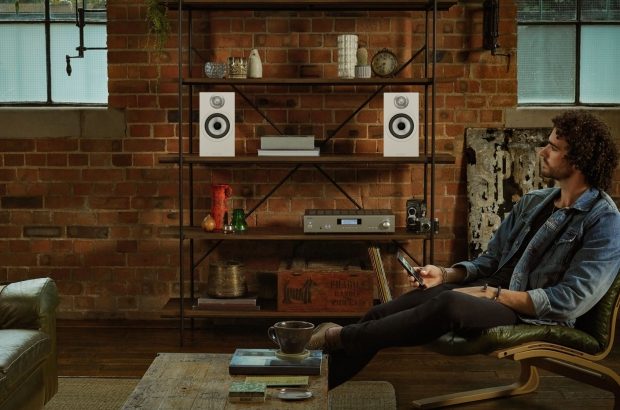 607 S2 Anniversary Edition – Matte White – Male Listening in Chair with Phone Front 1 – looking at speakers